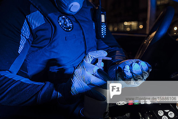 Polizist trägt Maske  Schutzhandschuhe und verwendet Desinfektionsmittel bei nächtlichen Notfalleinsätzen