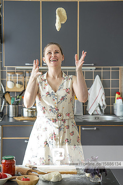 Porträt einer glücklichen Frau  die in der Küche Teig in die Luft wirft