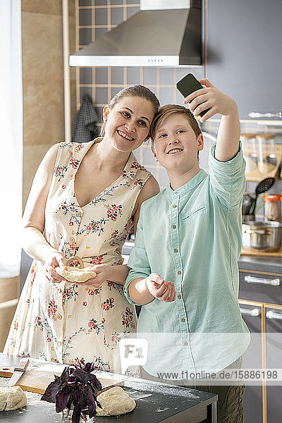 Mother and son taking selfie with smartphone in the kitchen