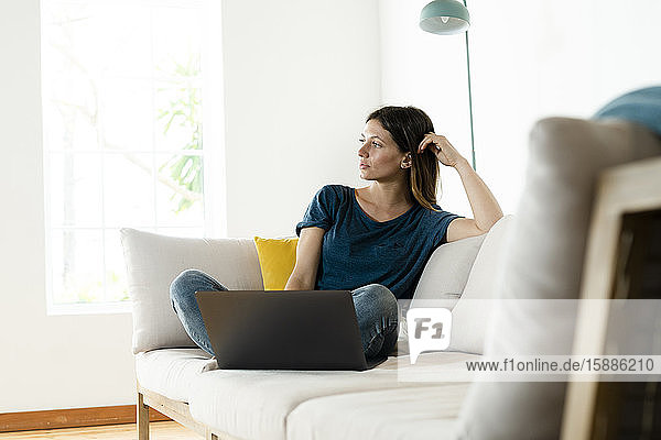 Junge Frau sitzt zu Hause auf der Couch mit Laptop
