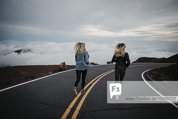 Rückansicht von Freunden  die gemeinsam auf der Strasse am Vulkan Haleakala laufen  Hawaii  Maui  USA