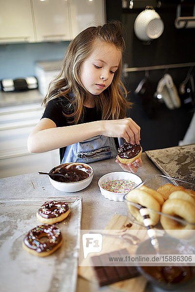 Porträt eines Mädchens  das selbstgebackene Krapfen mit Zuckergranulat dekoriert