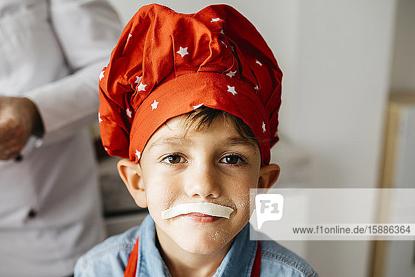Porträt eines verspielten Jungen mit Nudelschnurrbart-Attrappe in der heimischen Küche