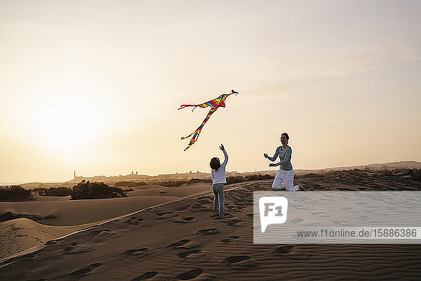 Mother and daughter flying kite in sand dunes at sunset  Gran Canaria  Spain