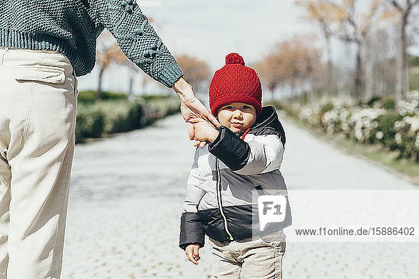 Portrait of little boy holding mother's hand wearing red bobble hat
