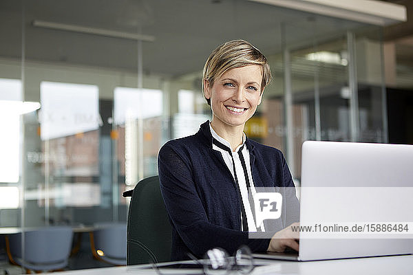 Porträt einer lächelnden Geschäftsfrau mit Laptop im Büro