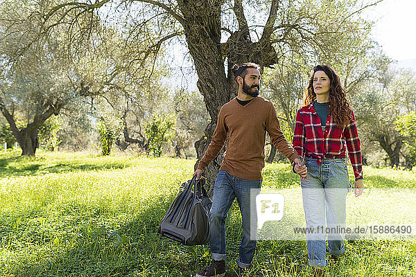 Couple with traveling bag walking hand in hand in the countryside