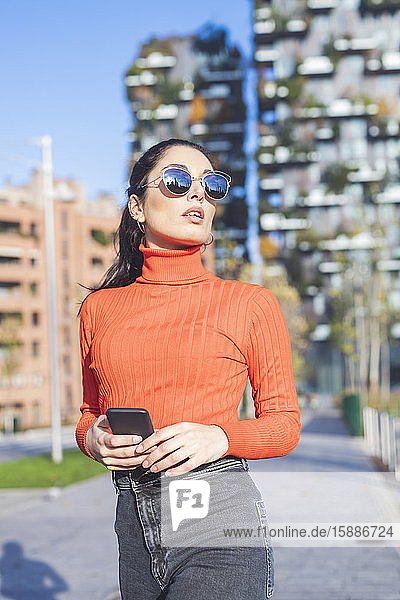 Schöne Frau mit Sonnenbrille und Smartphone in der Hand in der Stadt