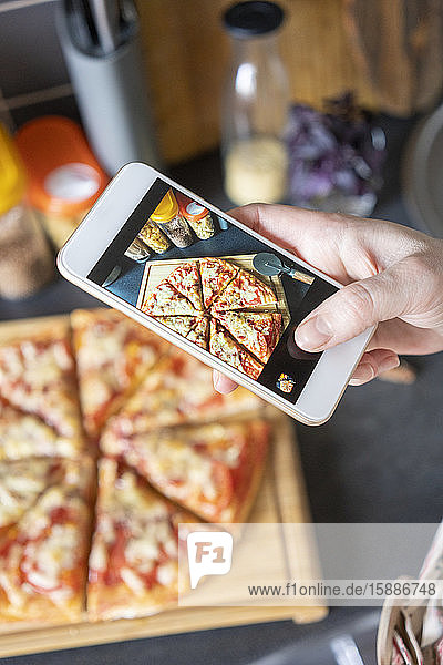 Frauenhand fotografiert hausgemachte Pizza mit Smartphone