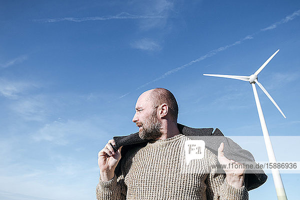 Bearded mature man against sky with wind wheel in the background