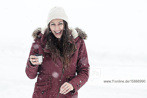 Portrait of laughing young woman with hot beverage in snow