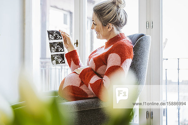 Pregnant woman holding ultrasound image at home