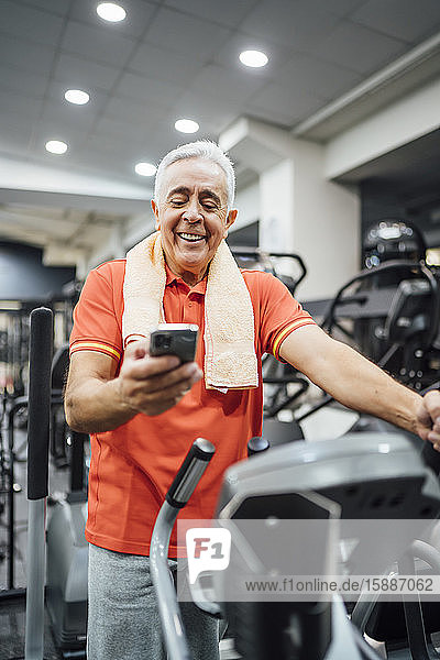 Smiling senior man having a break and using cell phone in gym