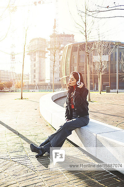 Schöne Frau sitzt auf einer Bank  benutzt ein Smartphone und hört Musik