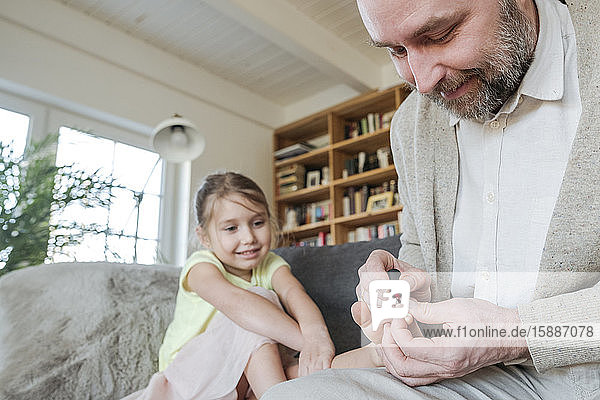 Father painting his daughter's toenails with red nail polish on the couch in living room