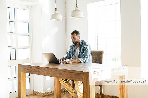 Junger Mann arbeitet zu Hause an seinem Laptop im Heimbüro im modernen Wohnzimmer