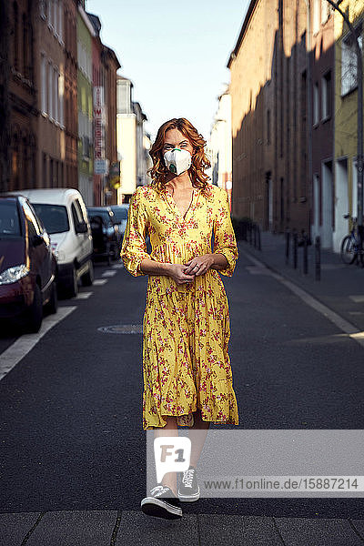Rothaarige Frau trägt eine FFP2-Gesichtsmaske und geht auf leerer Straße