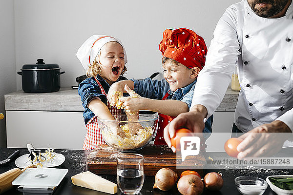 Glückliche Kinder beim Teigzubereiten mit dem Vater in der Küche zu Hause