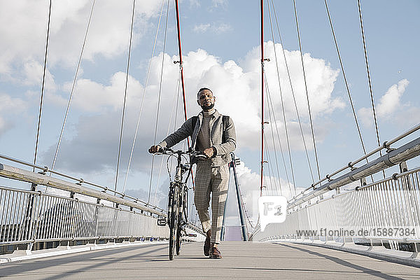 Stilvoller Mann mit Fahrrad auf einer Brücke