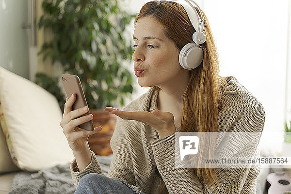 Junge Frau mit Kopfhörern und Smartphone beim Chatten zu Hause