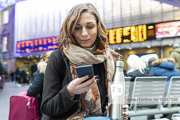 Frau  die am Bahnhof sitzt und ein Mobiltelefon benutzt