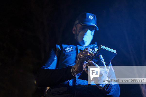 Policeman during emergency mission at night  taking notes  wearing protective gloves and mask