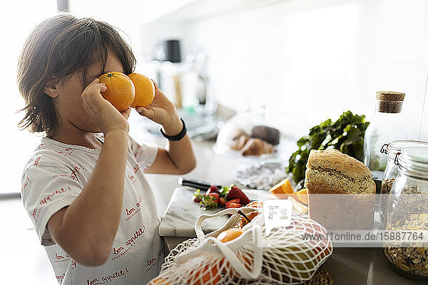 Junge in der Küche  der Augen mit Orangen bedeckt