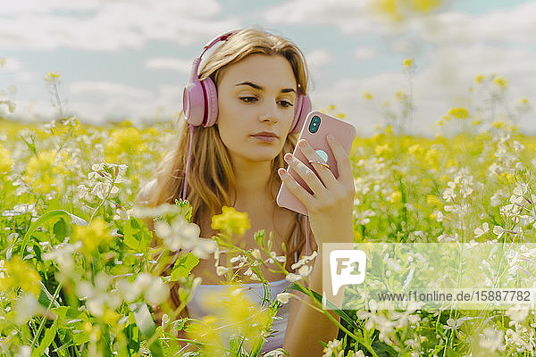 Junge Frau mit Kopfhörer und Smartphone auf einer Blumenwiese im Frühling