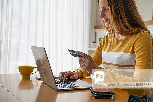 Junge Frau mit Kreditkarte mit Laptop zu Hause