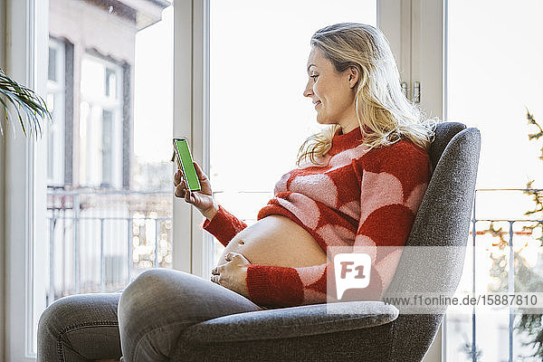 Schwangere  die zu Hause auf ihr Handy schaut