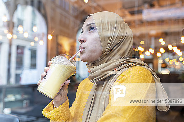 Junge Frau mit Hijab  die in einem Café Smoothie trinkt