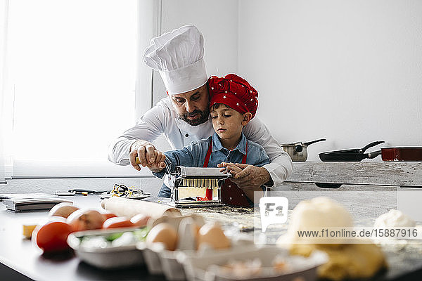 Vater und Sohn machen hausgemachte Nudeln mit der Nudelmaschine in der heimischen Küche