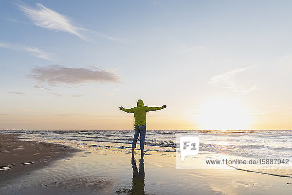 Senior man with arms outstretched standing on shore at beach during sunset  North Sea Coast  Flanders  Belgium