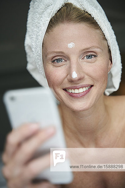 Portrait of beautiful woman with head wrapped in a towel holding smartphone