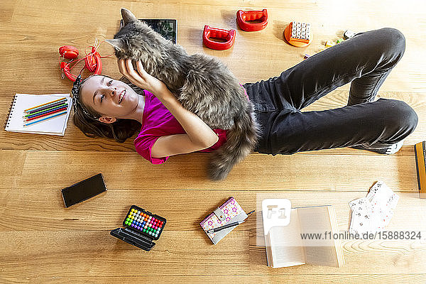 Auf dem Boden liegendes Mädchen  kuschelnde Katze  umgeben von Spielgeräten