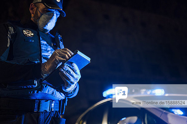 Polizist bei nächtlichen Notfalleinsätzen  macht Notizen  trägt Schutzhandschuhe und Maske