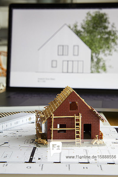 Architekturmodell des Wohneigentums auf Bauplan  Laptop im Hintergrund