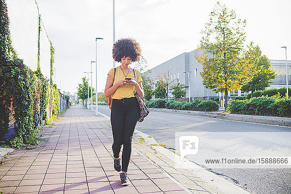 Young woman with afro hairdo using smartphone in the city