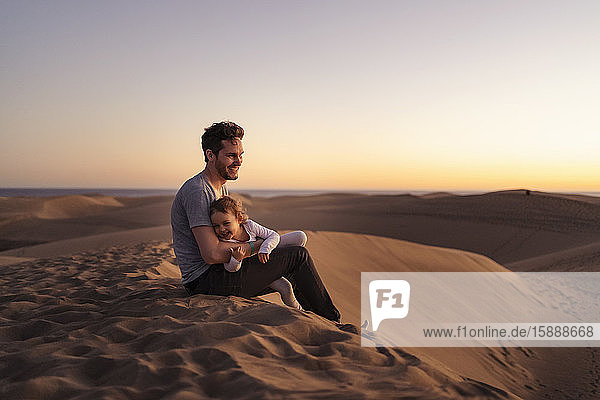 Glücklicher Vater sitzt mit seiner Tochter bei Sonnenuntergang in den Sanddünen  Gran Canaria  Spanien