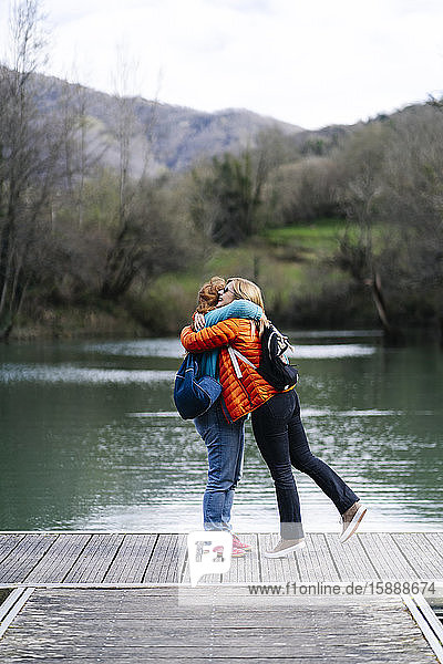 Zwei glückliche Frauen mit Rucksäcken stehen auf einem Steg und umarmen sich  Stausee Valdemurio  Asturien  Spanien