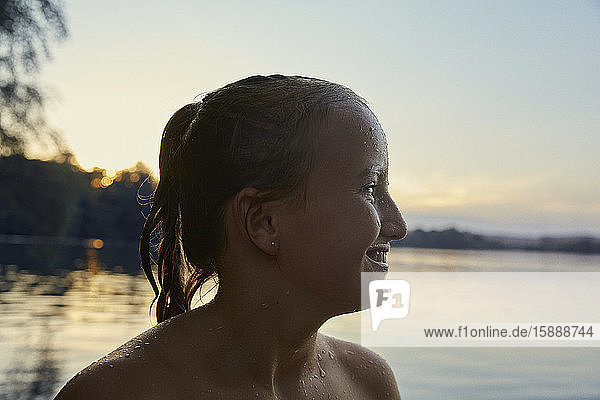 Profil eines glücklichen nassen Mädchens vor einem See in der Abenddämmerung