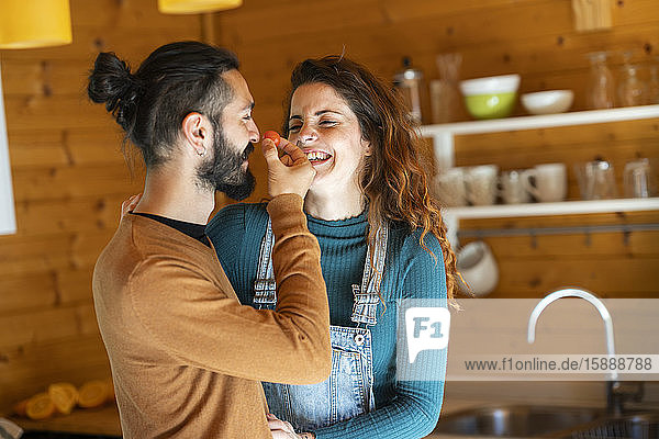 Glückliches junges Paar spielt mit einer Kirschtomate in einer Holzhütte