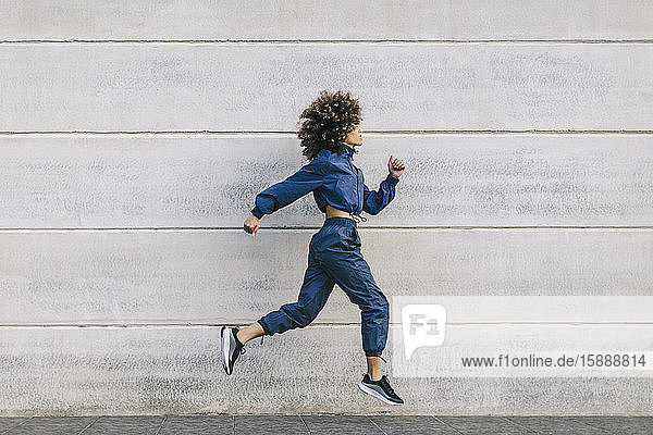 Stylish young woman running along concrete wall
