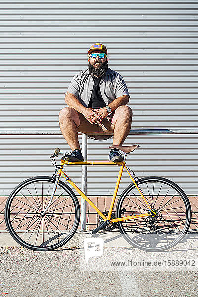 Bildnis eines bärtigen Mannes mit gelbem Fixie-Fahrrad auf einem Geländer sitzend
