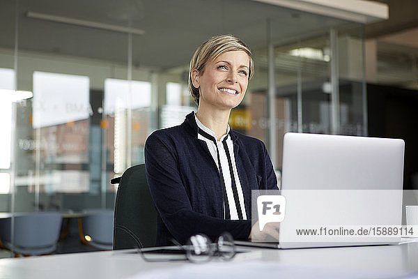 Lächelnde Geschäftsfrau benutzt Laptop im Büro