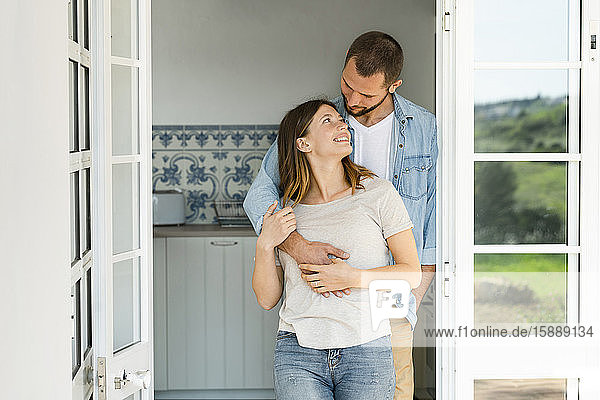 Attractive young couple standing in the door together at home and smiling at each other
