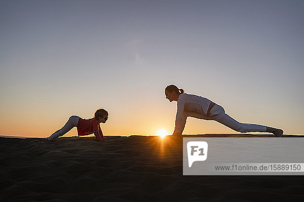 Mother and daughter practicing yoga in sand dunes at sunset  Gran Canaria  Spain