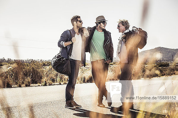 Drei Männer mit Reisetaschen auf der Landstraße stehend