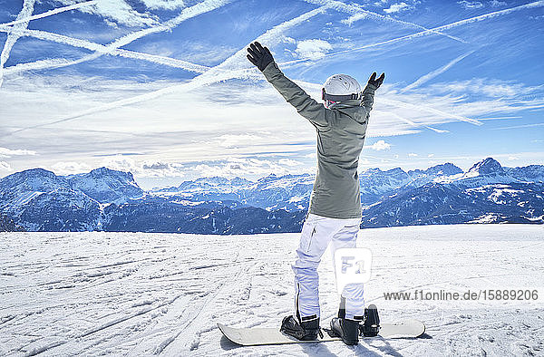 Reife Frau mit Snowboard auf der Skipiste mit erhobenen Armen
