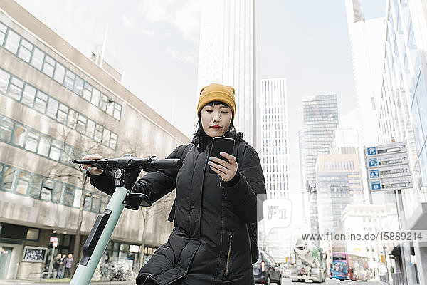 Frau mit Roller mit Smartphone in der Stadt  Frankfurt  Deutschland